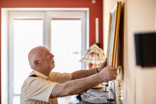 An elderly man hangs an insured painting on a wall